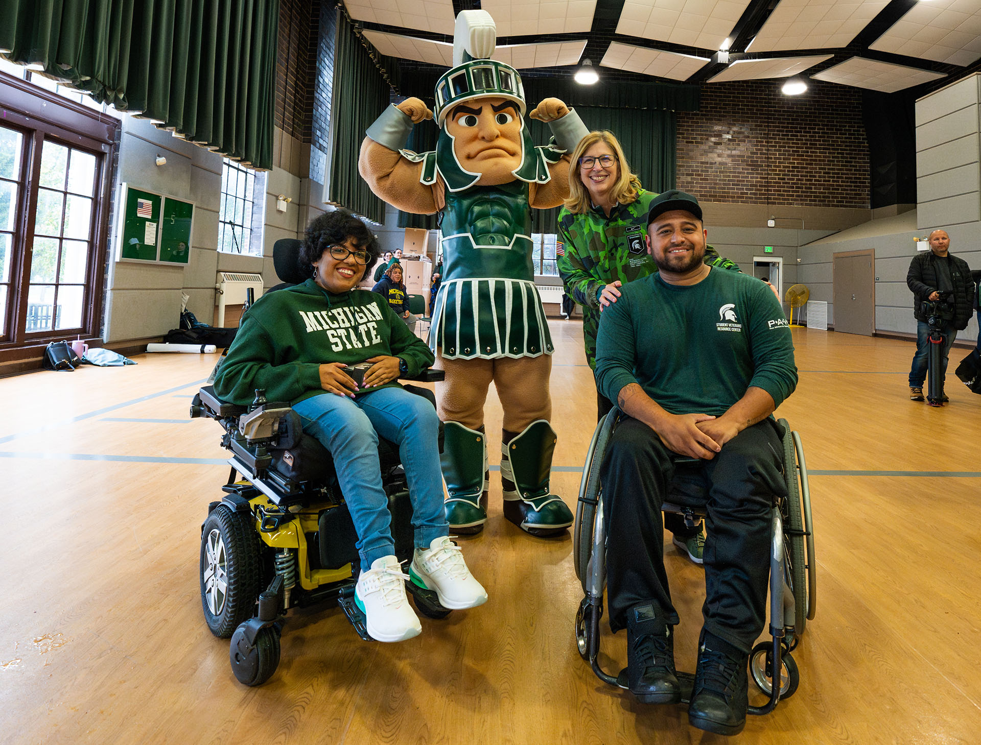 Sparty and interim president with two people in wheelchairs at the Alex's Great State Race welcome reception