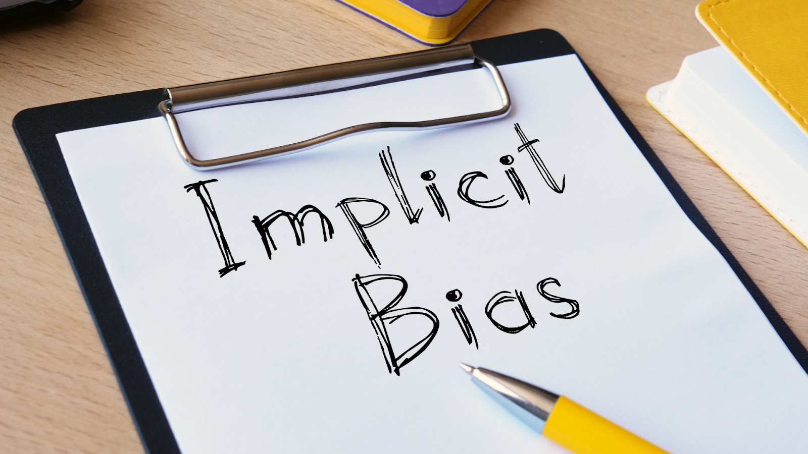 A clipboard with the words implicit bias on a piece a paper