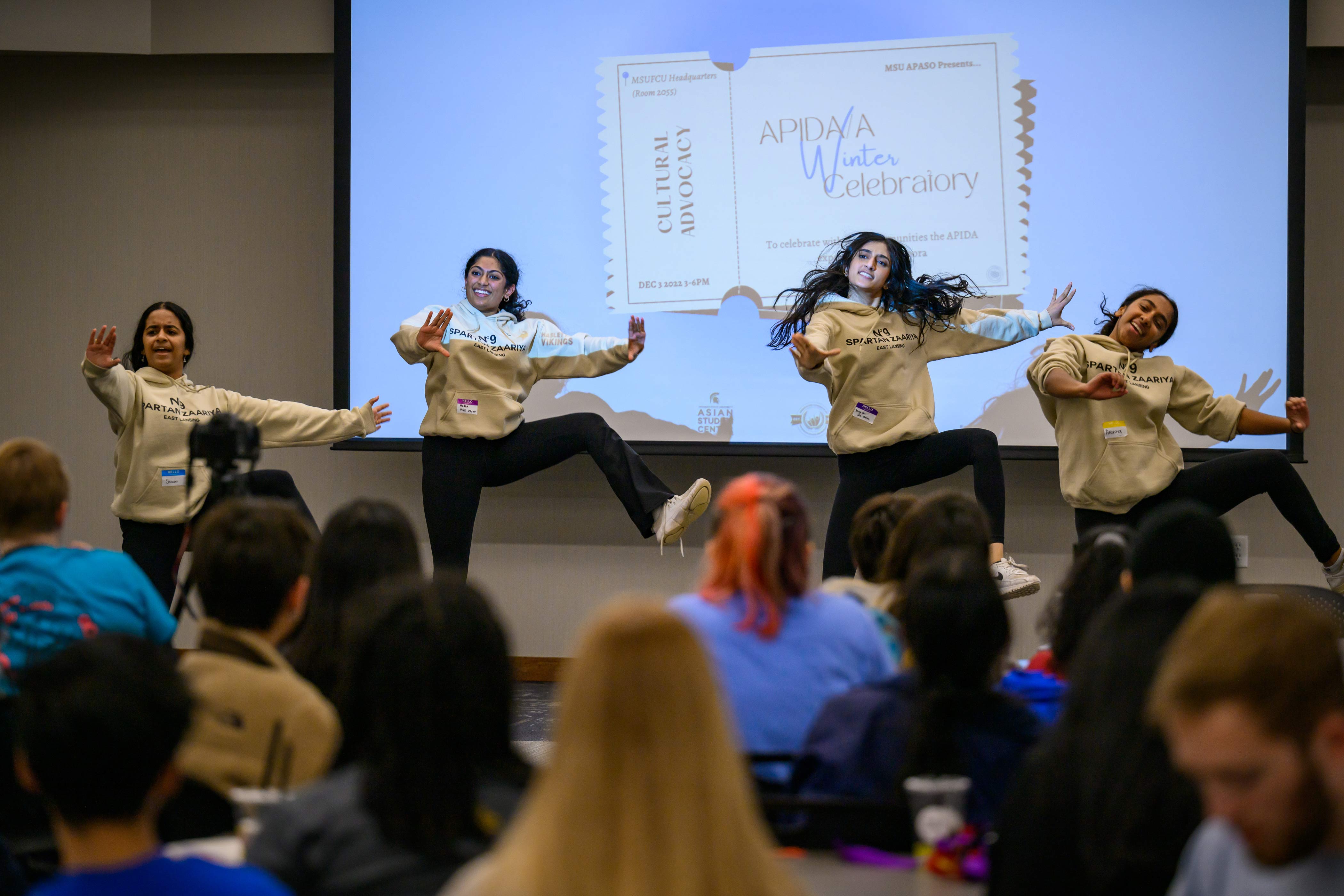 Four students performing a dance in front of APIDA/A Winter Celebratory projection