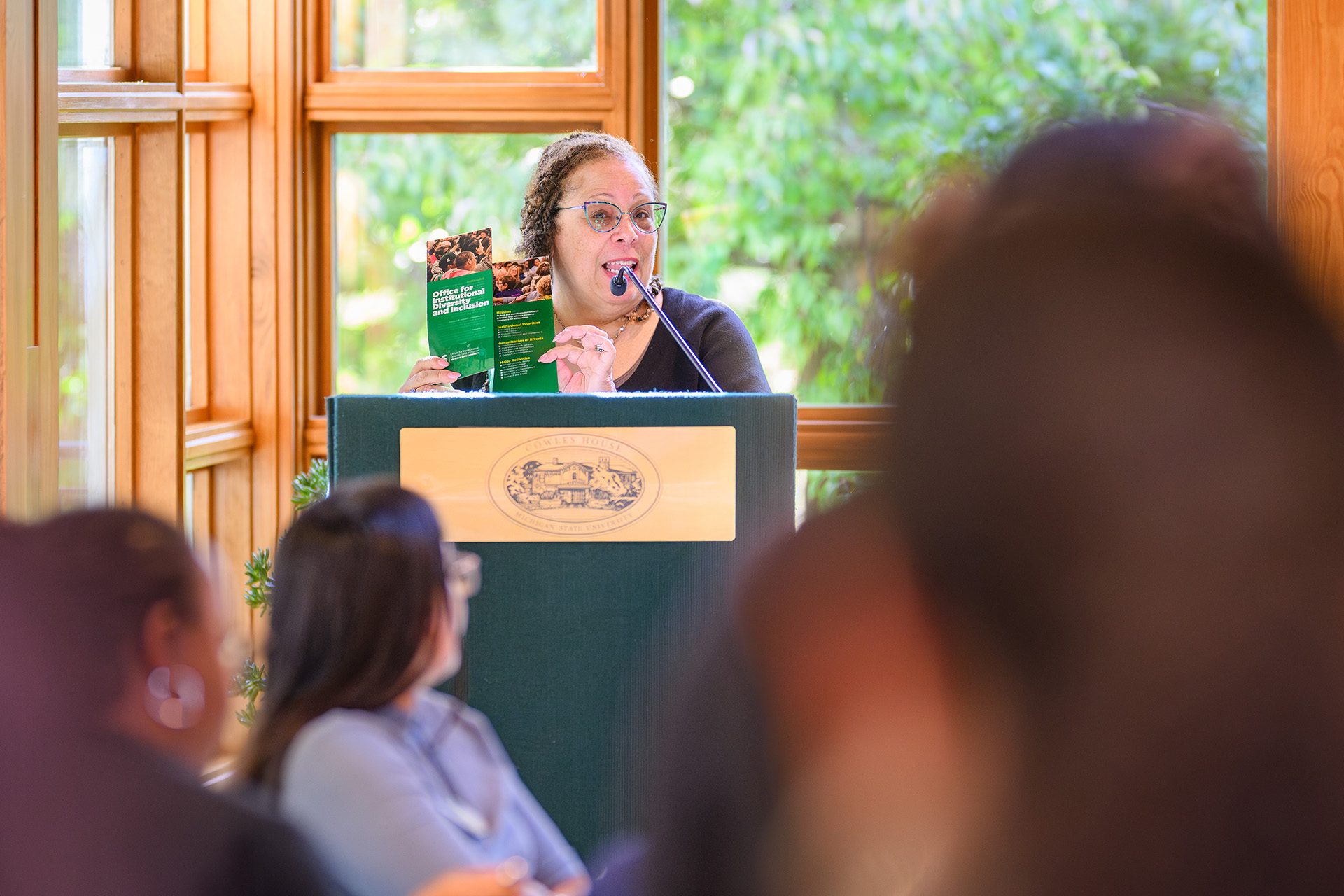 IDI speaker offers welcome remarks at the lectern holding an office brochure