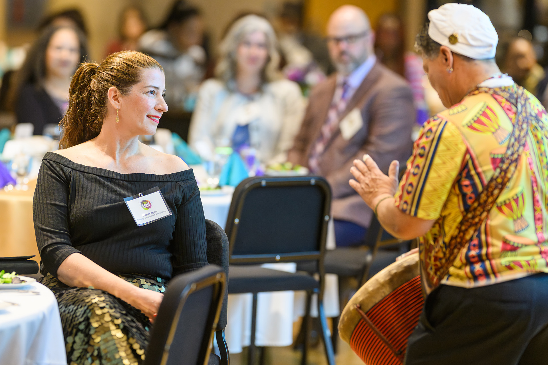 a woman smiles as she watches a drummer in front of her