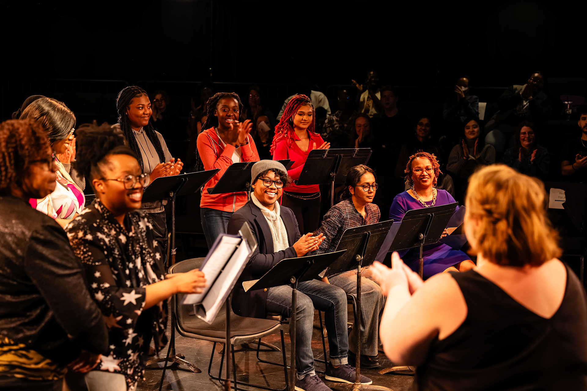 theatre director applauds the performers on stage who are seated and standing