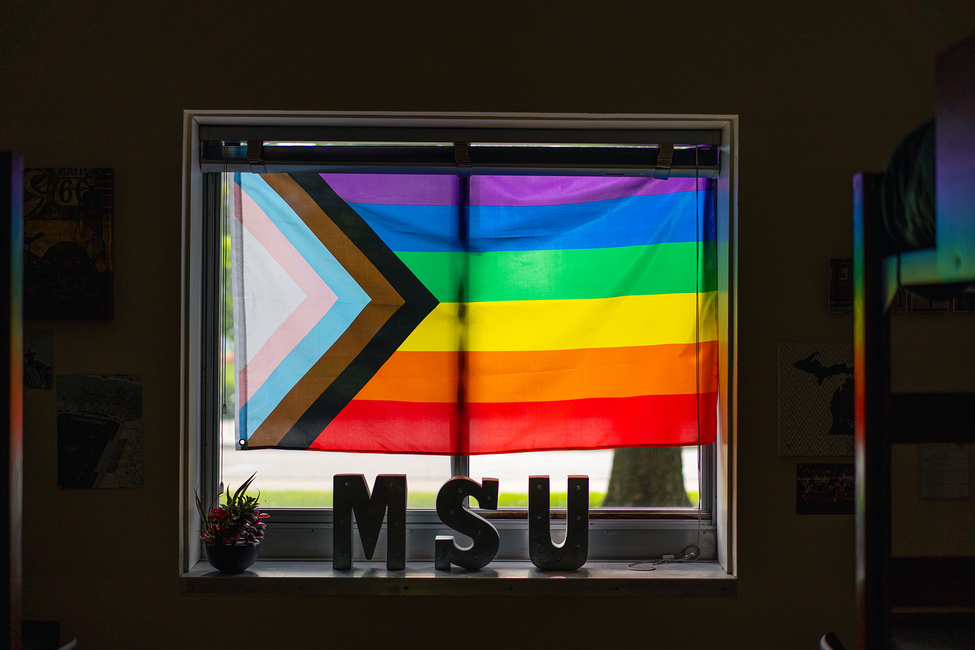 progressive pride flag in a window with MSU block letters on the sill