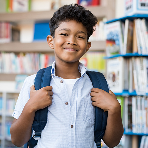 boy with a backpack smiling in the library full of books