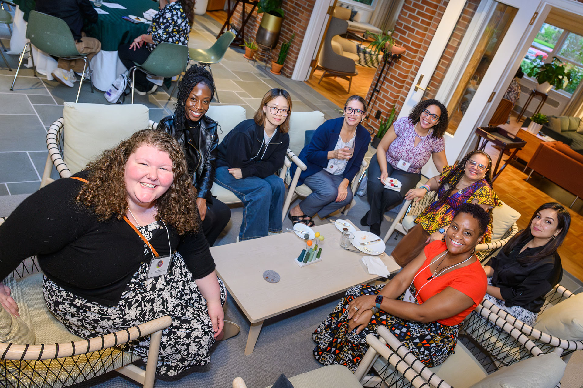 Eight women of color sitting around a coffee table smiling at the camera